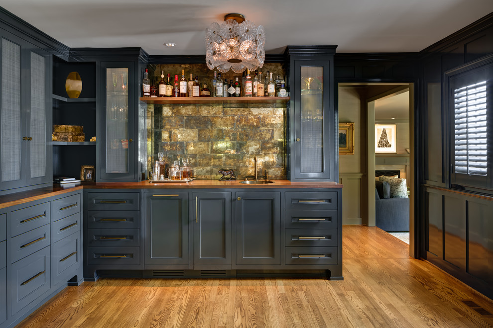 Cette image montre un bar de salon avec évier traditionnel en L avec un évier posé, un placard avec porte à panneau encastré, des portes de placard grises, un plan de travail en bois, un sol en bois brun et un plan de travail marron.