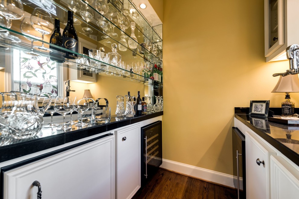 This is an example of a small traditional galley home bar in Dallas with a submerged sink, raised-panel cabinets, white cabinets, granite worktops, mirror splashback, medium hardwood flooring and brown floors.