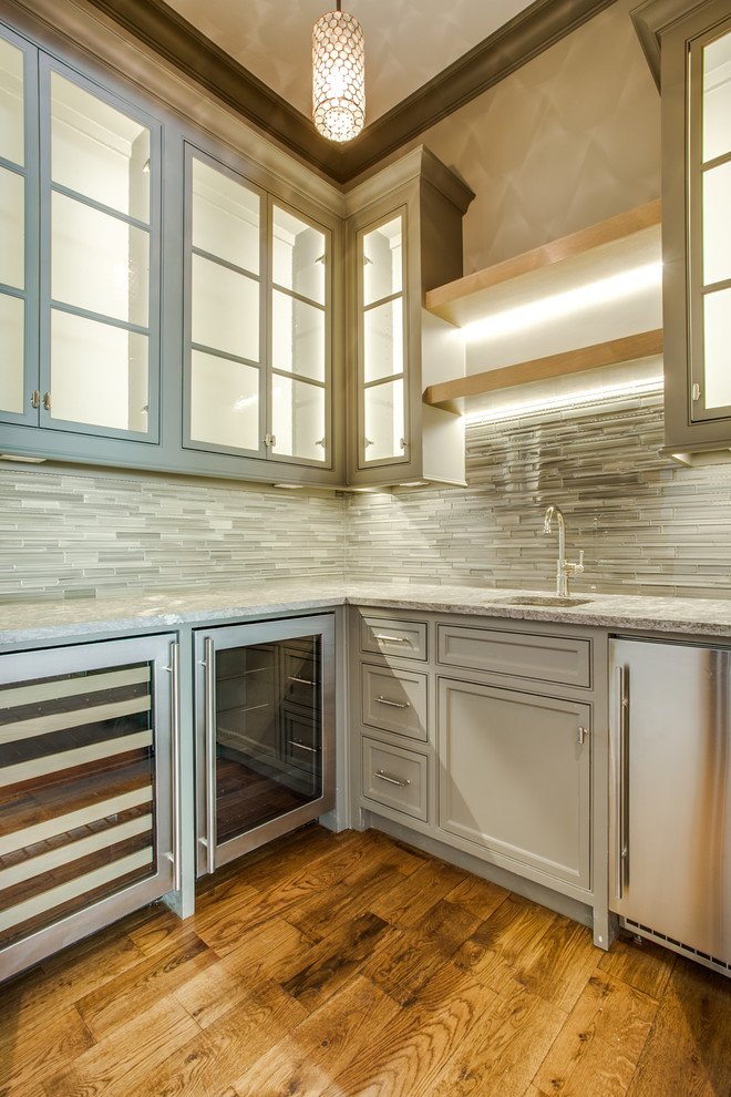 Klassische Hausbar mit Küchenrückwand in Grau, Rückwand aus Stäbchenfliesen, braunem Holzboden, Kassettenfronten und beigen Schränken in Dallas