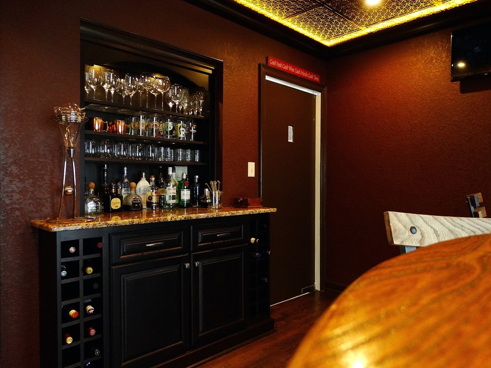 Ispirazione per un bancone bar tradizionale di medie dimensioni con ante con bugna sagomata, ante nere, top in granito e pavimento in legno massello medio