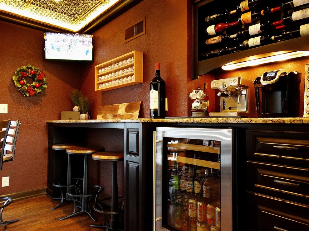 Ispirazione per un bancone bar classico di medie dimensioni con ante con bugna sagomata, ante nere, top in granito e pavimento in legno massello medio