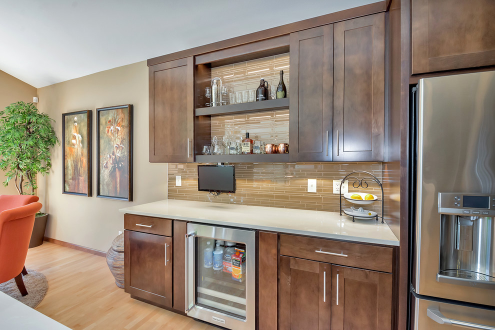 Large traditional home bar in Seattle with shaker cabinets, medium wood cabinets, beige splashback, glass tiled splashback and light hardwood flooring.
