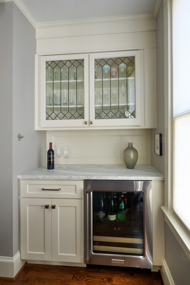 Inspiration for a small traditional single-wall wet bar in Seattle with shaker cabinets, white cabinets, dark hardwood flooring, no sink, marble worktops, white splashback, wood splashback, brown floors and white worktops.