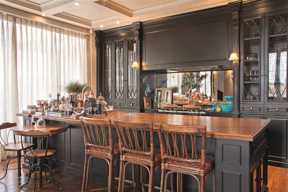 Diseño de bar en casa con barra de bar de galera mediterráneo con armarios con paneles empotrados, puertas de armario negras, salpicadero con efecto espejo y suelo de madera en tonos medios