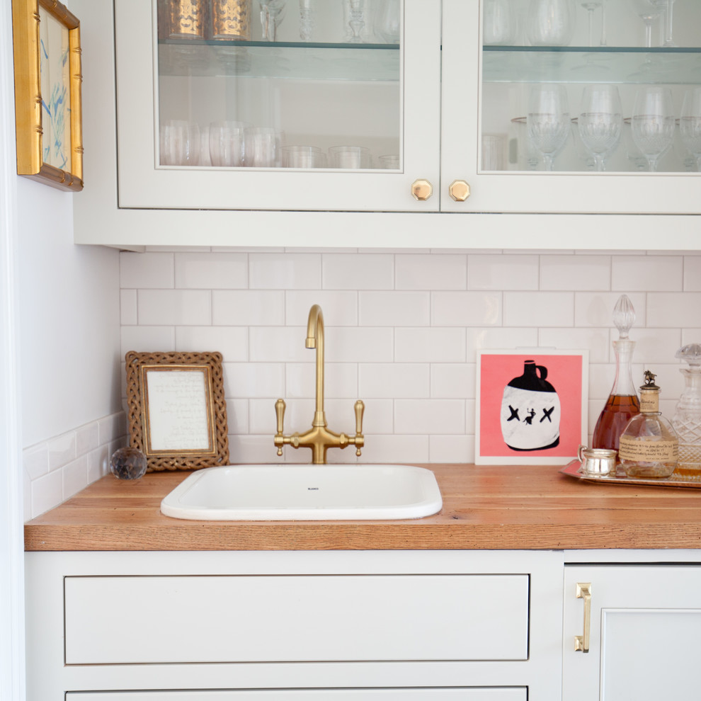 Klassisk inredning av en liten parallell hemmabar med vask, med en nedsänkt diskho, luckor med infälld panel, vita skåp, träbänkskiva, vitt stänkskydd, stänkskydd i keramik och skiffergolv