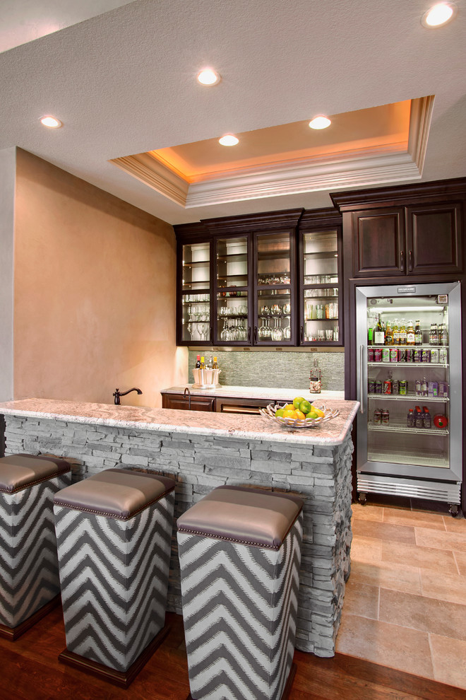 Seated home bar - traditional seated home bar idea in Orange County with glass-front cabinets, dark wood cabinets, gray backsplash and stone tile backsplash