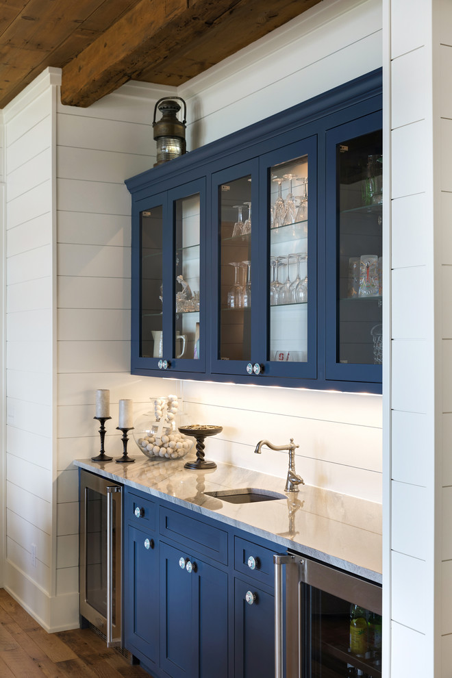 Idee per un angolo bar con lavandino stile marinaro con lavello sottopiano, ante blu, top in marmo, paraspruzzi bianco, paraspruzzi in legno, pavimento marrone, ante di vetro e parquet scuro