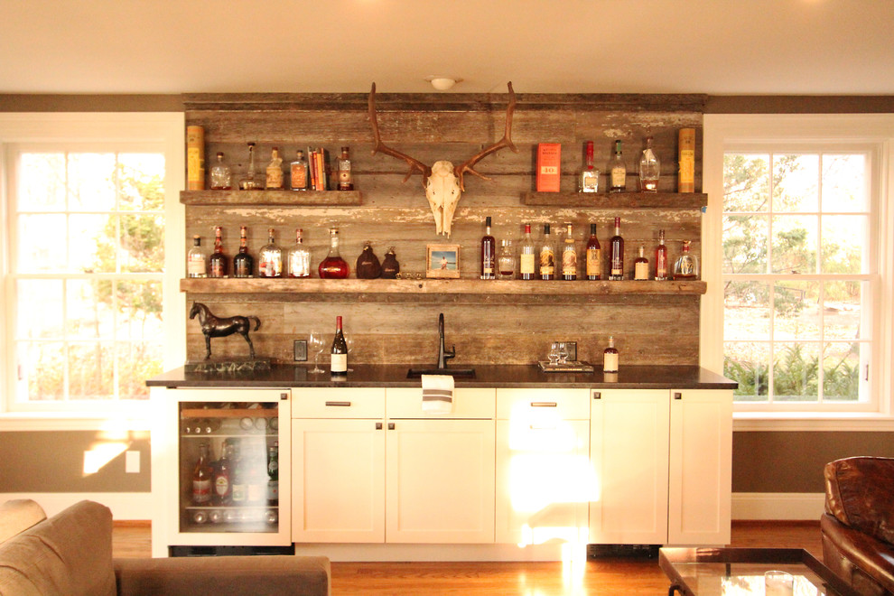 Inredning av en klassisk liten linjär hemmabar med vask, med en undermonterad diskho, luckor med infälld panel, vita skåp, granitbänkskiva, grått stänkskydd, stänkskydd i trä, mellanmörkt trägolv och brunt golv