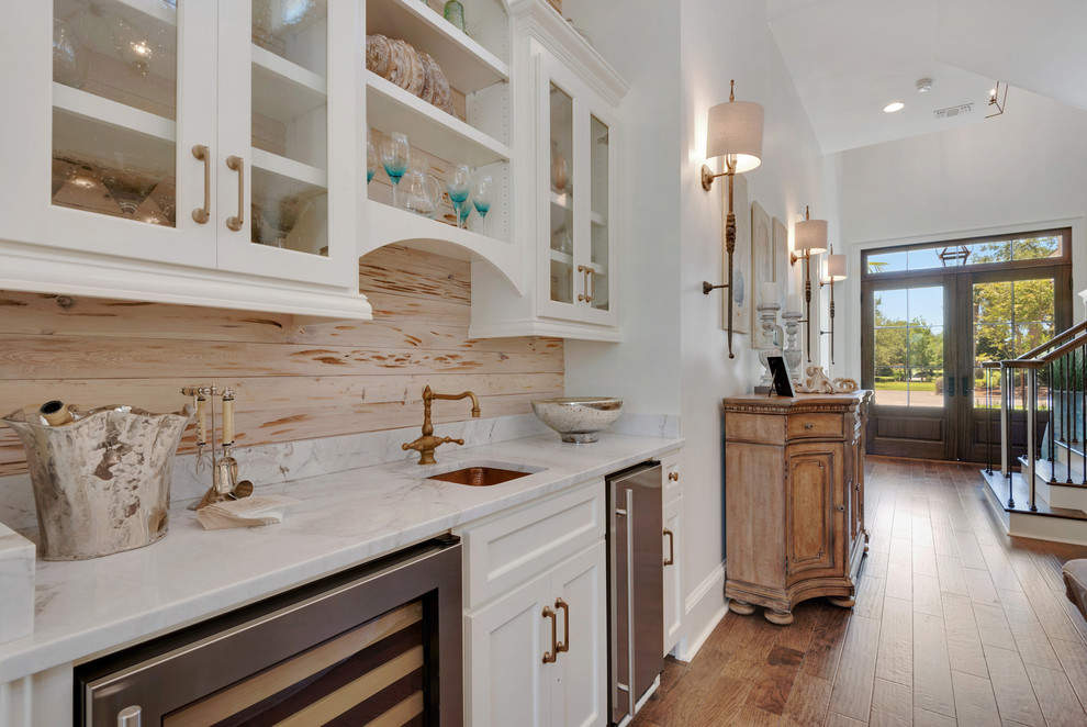 Exempel på en liten maritim linjär hemmabar med vask, med en undermonterad diskho, luckor med glaspanel, vita skåp, marmorbänkskiva, flerfärgad stänkskydd, stänkskydd i sten och mellanmörkt trägolv