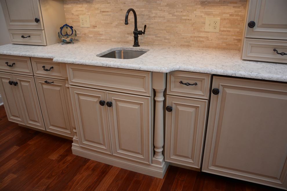 Photo of a small classic single-wall wet bar in Baltimore with a submerged sink, raised-panel cabinets, beige cabinets, engineered stone countertops, beige splashback, stone tiled splashback, dark hardwood flooring, brown floors and white worktops.
