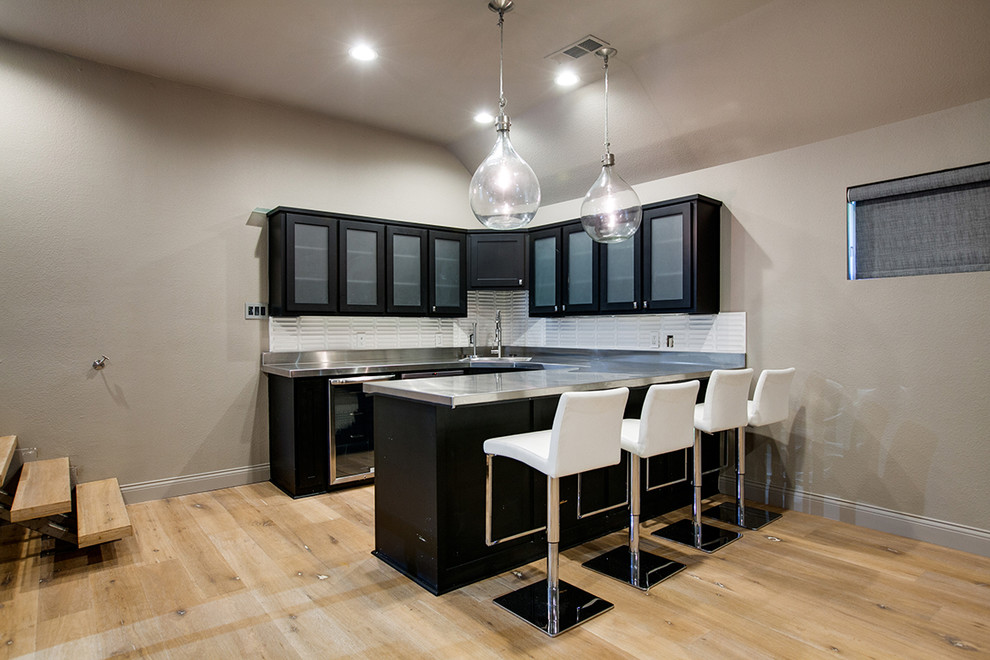 Medium sized contemporary galley breakfast bar in Dallas with a submerged sink, glass-front cabinets, black cabinets, stainless steel worktops, white splashback, ceramic splashback and light hardwood flooring.