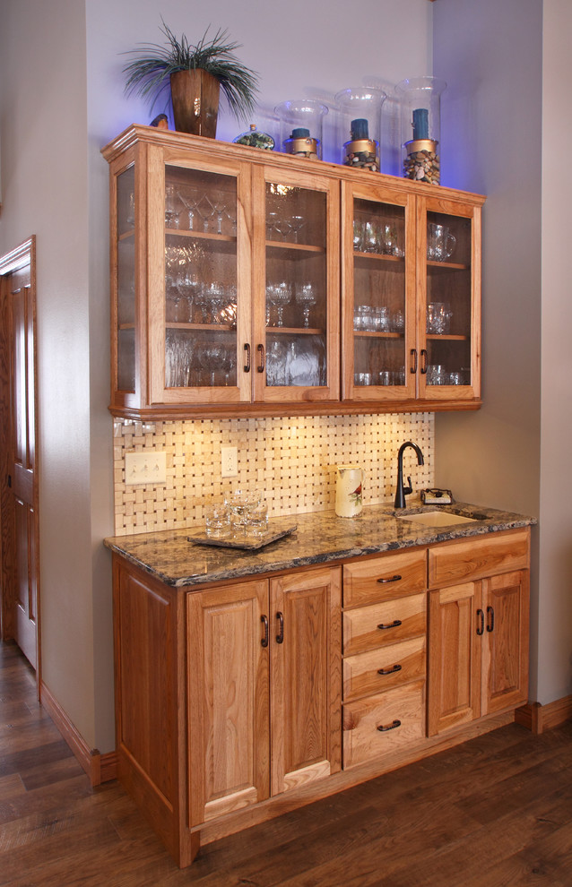 Photo of a small classic single-wall wet bar in Minneapolis with a submerged sink, raised-panel cabinets, medium wood cabinets, engineered stone countertops, beige splashback, mosaic tiled splashback and light hardwood flooring.