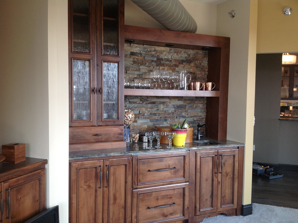 Example of a small mountain style single-wall carpeted wet bar design in Milwaukee with an undermount sink, recessed-panel cabinets, dark wood cabinets, granite countertops and slate backsplash
