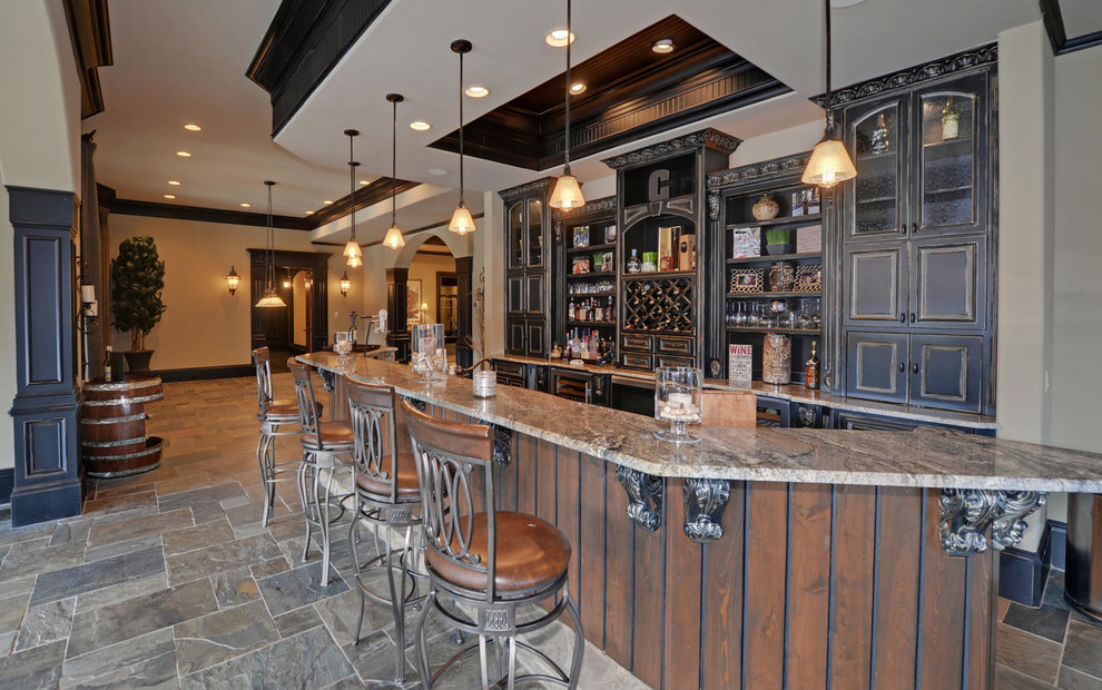 Cette photo montre un grand bar de salon parallèle montagne en bois vieilli avec des tabourets, un placard avec porte à panneau surélevé, un plan de travail en granite, un sol en ardoise et un sol gris.