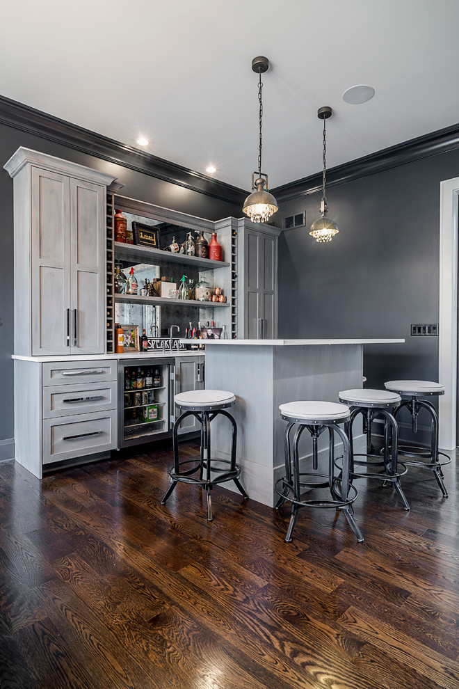 This is an example of a medium sized classic single-wall wet bar in Chicago with a submerged sink, recessed-panel cabinets, grey cabinets, engineered stone countertops, mirror splashback and medium hardwood flooring.