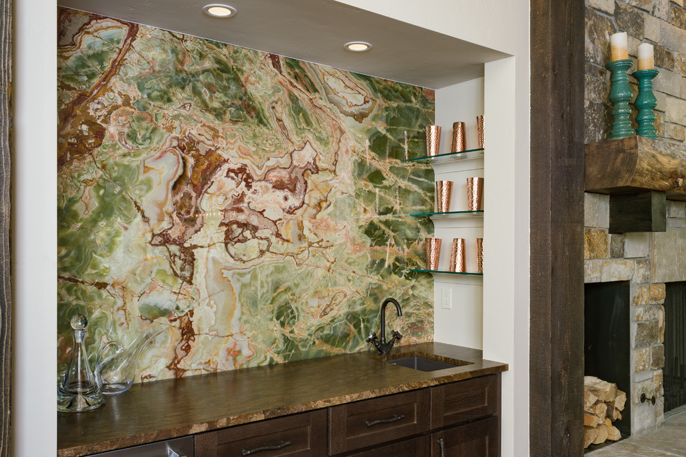 Cette image montre un bar de salon avec évier linéaire chalet avec un évier encastré, un plan de travail en granite, une crédence verte, une crédence en dalle de pierre et un sol en bois brun.