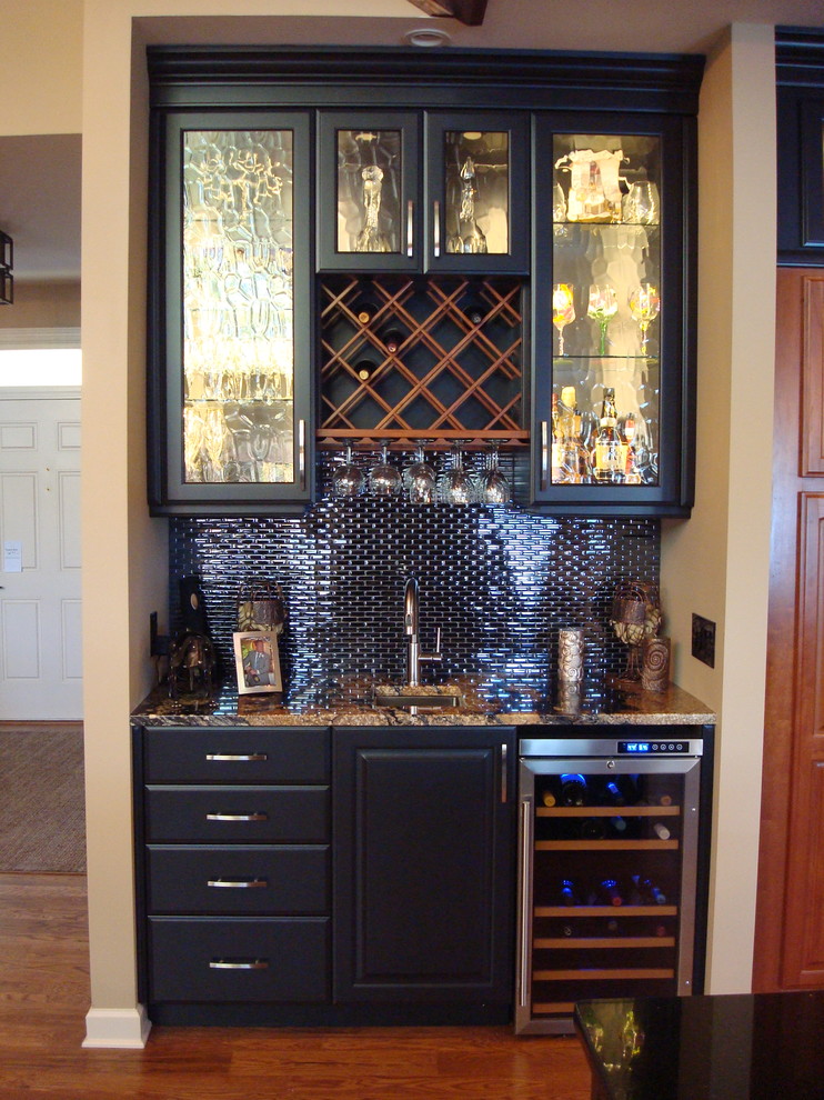 Inspiration for a large timeless l-shaped medium tone wood floor and brown floor wet bar remodel in Other with an undermount sink, raised-panel cabinets, black cabinets, granite countertops, black backsplash and glass tile backsplash