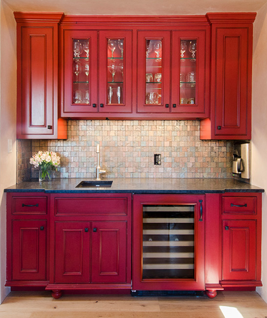 Inredning av en klassisk mellanstor linjär hemmabar med vask, med en undermonterad diskho, luckor med glaspanel, röda skåp, granitbänkskiva, flerfärgad stänkskydd, stänkskydd i glaskakel och mellanmörkt trägolv