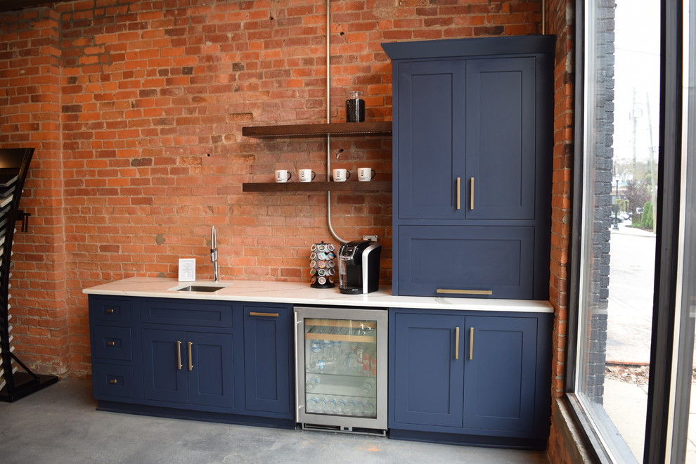 Cette image montre un bar de salon avec un évier encastré, un placard à porte shaker, des portes de placard bleues, un plan de travail en quartz modifié et sol en béton ciré.