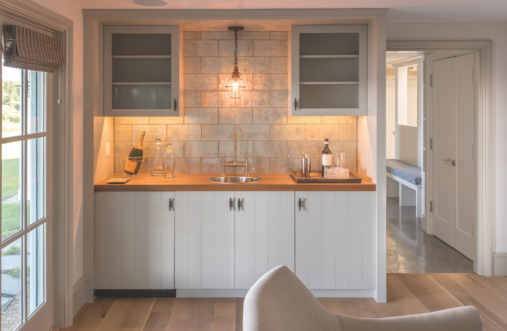 Mid-sized beach style single-wall light wood floor and brown floor wet bar photo in Portland Maine with a drop-in sink, flat-panel cabinets, white cabinets, wood countertops, gray backsplash and metal backsplash