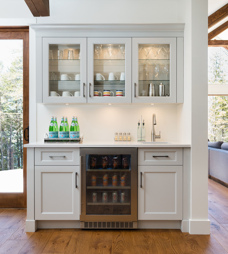 This is an example of a large classic single-wall home bar in Montreal with shaker cabinets, grey cabinets, engineered stone countertops, white splashback, metro tiled splashback and medium hardwood flooring.