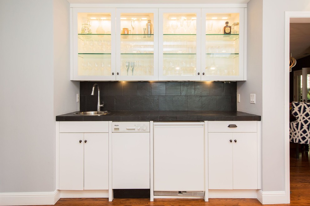This is an example of a medium sized classic single-wall wet bar in San Francisco with a built-in sink, glass-front cabinets, white cabinets, black splashback, slate splashback, medium hardwood flooring and brown floors.