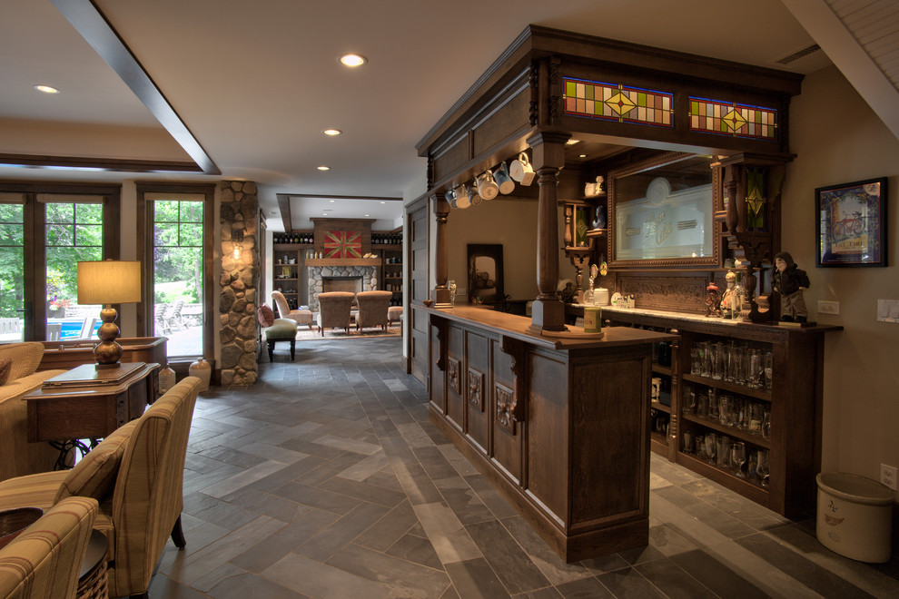 Ejemplo de bar en casa con barra de bar en U tradicional grande con armarios abiertos, puertas de armario de madera en tonos medios y suelo de pizarra