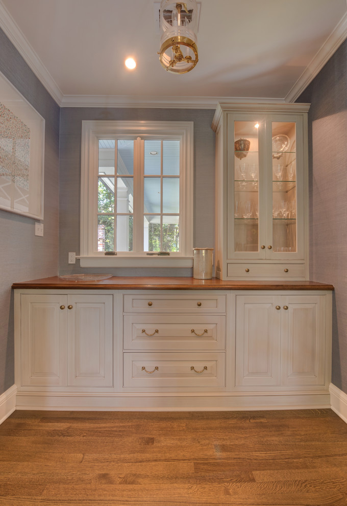 Example of a small classic galley medium tone wood floor and brown floor home bar design in New Orleans with raised-panel cabinets, white cabinets and wood countertops