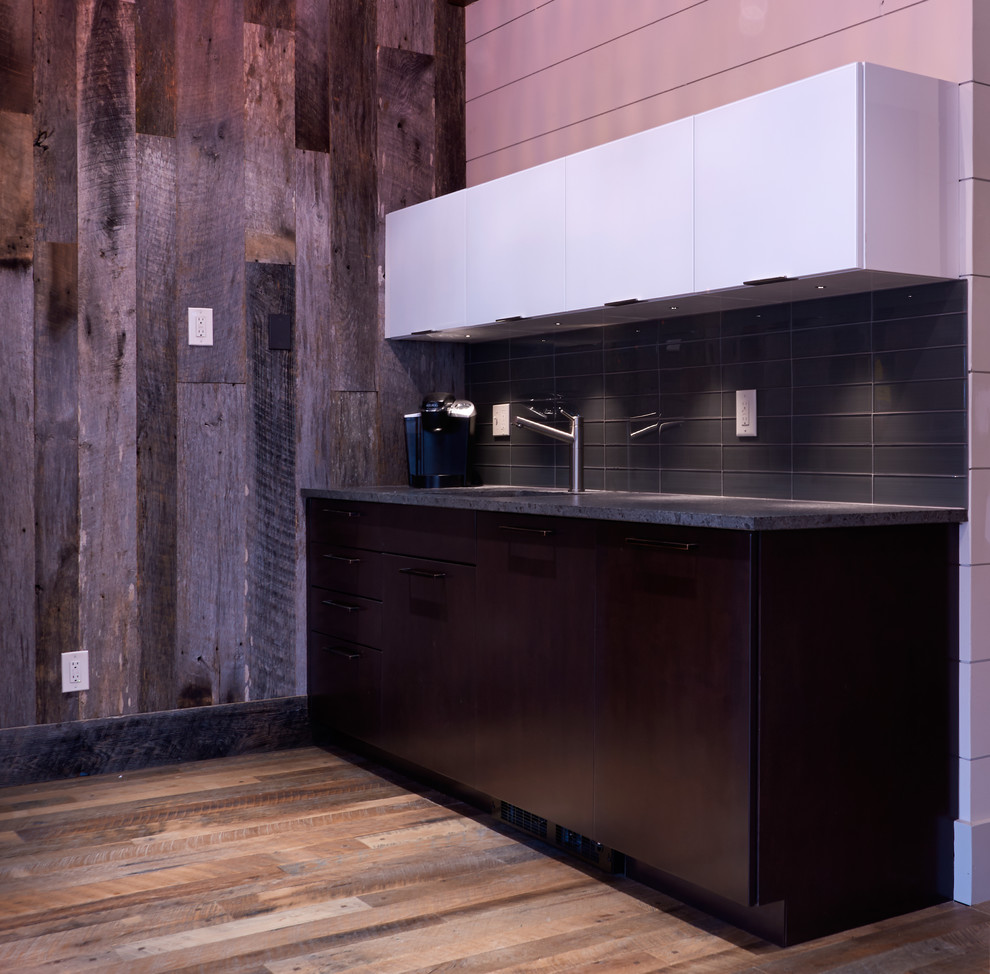 Inredning av en modern mellanstor svarta linjär svart hemmabar med vask, med en undermonterad diskho, släta luckor, skåp i mörkt trä, granitbänkskiva, svart stänkskydd, mellanmörkt trägolv och brunt golv