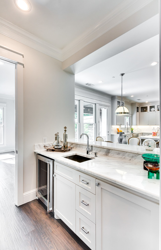 Klassisk inredning av en vita vitt hemmabar med vask, med en undermonterad diskho, skåp i shakerstil, vita skåp, marmorbänkskiva, vitt stänkskydd, mörkt trägolv och brunt golv