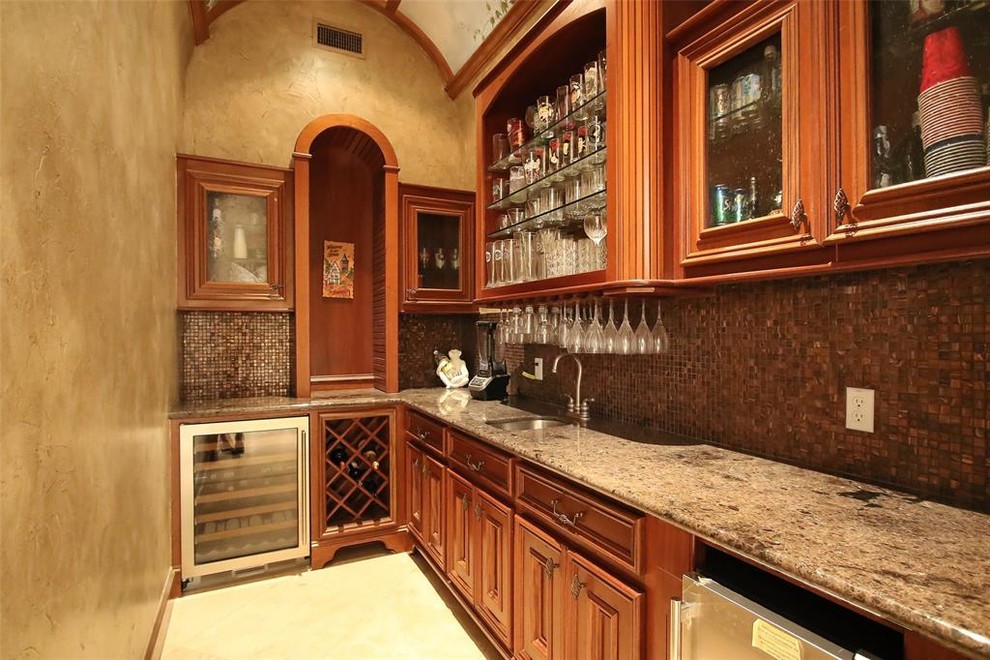 Example of a huge tuscan l-shaped travertine floor and beige floor wet bar design in Houston with an undermount sink, glass-front cabinets, medium tone wood cabinets, granite countertops, multicolored backsplash, glass tile backsplash and black countertops