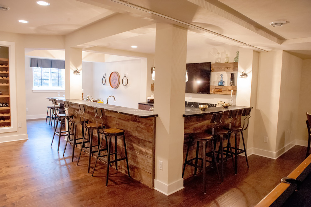 Huge transitional u-shaped medium tone wood floor and brown floor seated home bar photo in Milwaukee with an undermount sink, soapstone countertops and black countertops