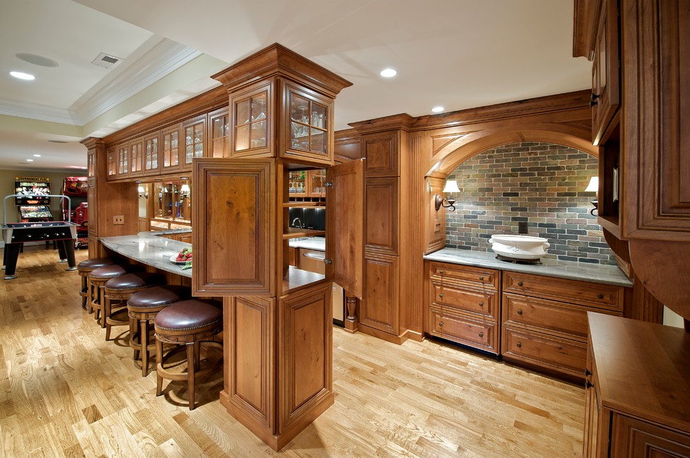 This is an example of a large traditional u-shaped breakfast bar in Philadelphia with a submerged sink, glass-front cabinets, medium wood cabinets, marble worktops, black splashback and light hardwood flooring.