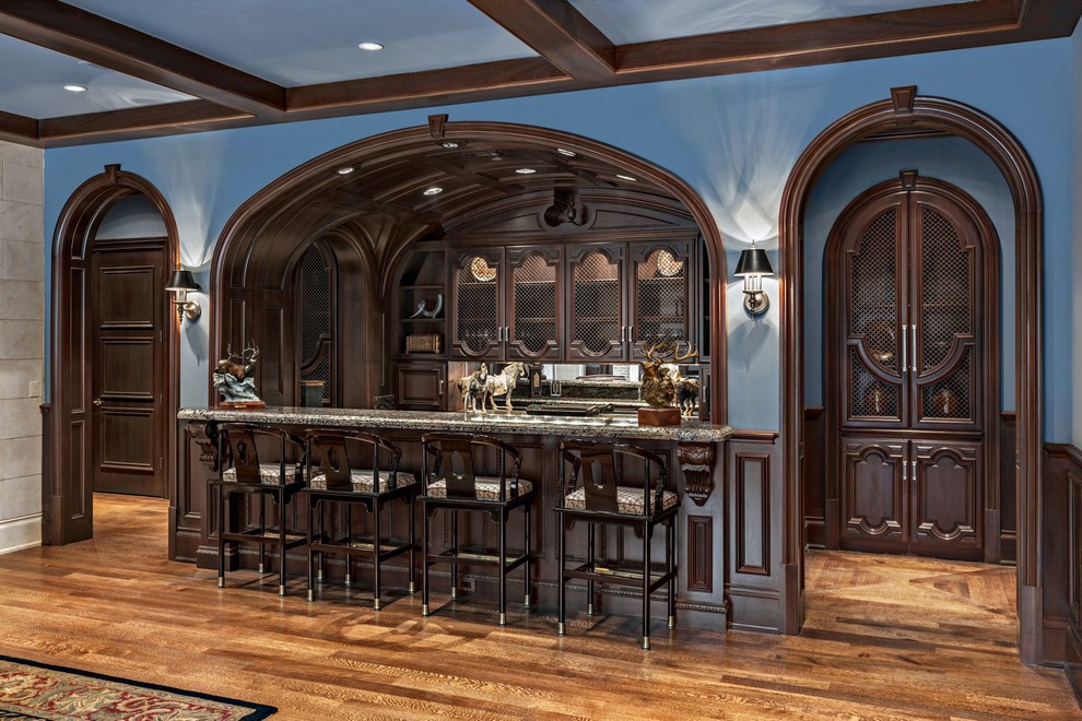 Große Klassische Hausbar in U-Form mit Bartheke, dunklen Holzschränken, Granit-Arbeitsplatte und braunem Holzboden in Dallas