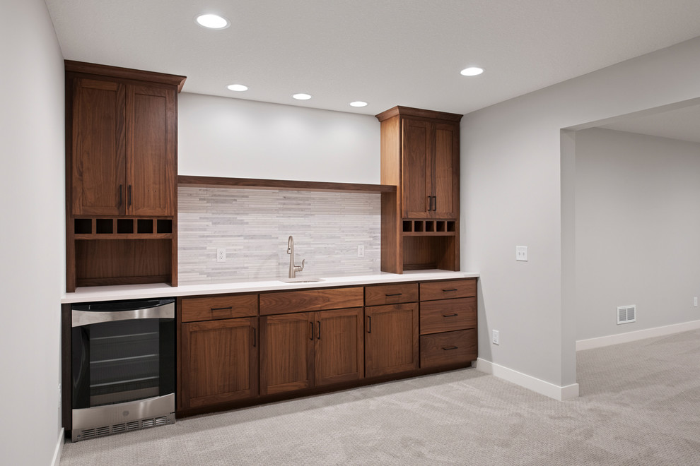 This is an example of a large classic single-wall wet bar in Minneapolis with a submerged sink, shaker cabinets, dark wood cabinets, granite worktops, grey splashback, ceramic splashback, carpet, grey floors and white worktops.