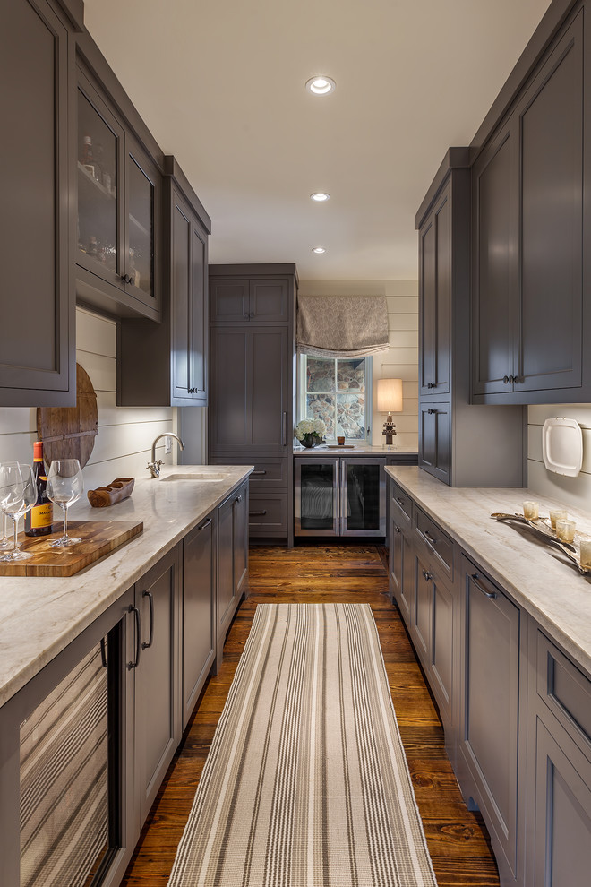 Exempel på en stor lantlig grå parallell grått hemmabar med vask, med en undermonterad diskho, grå skåp, brunt golv, skåp i shakerstil, marmorbänkskiva, vitt stänkskydd, stänkskydd i trä och mörkt trägolv