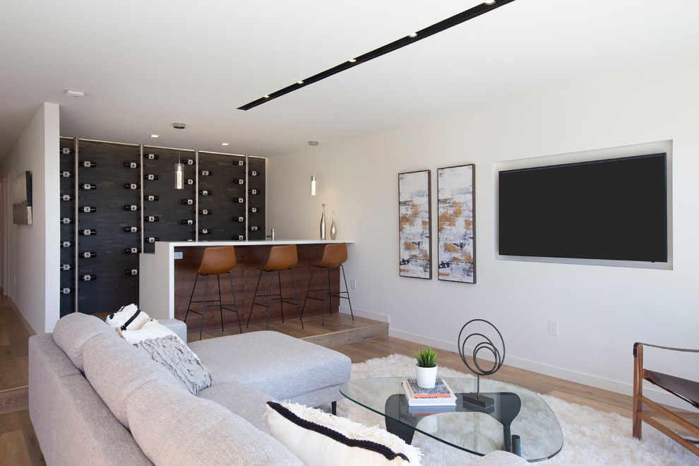 Cette image montre un bar de salon parallèle design en bois brun avec des tabourets, une crédence noire, un sol en bois brun, un sol marron et un plan de travail blanc.
