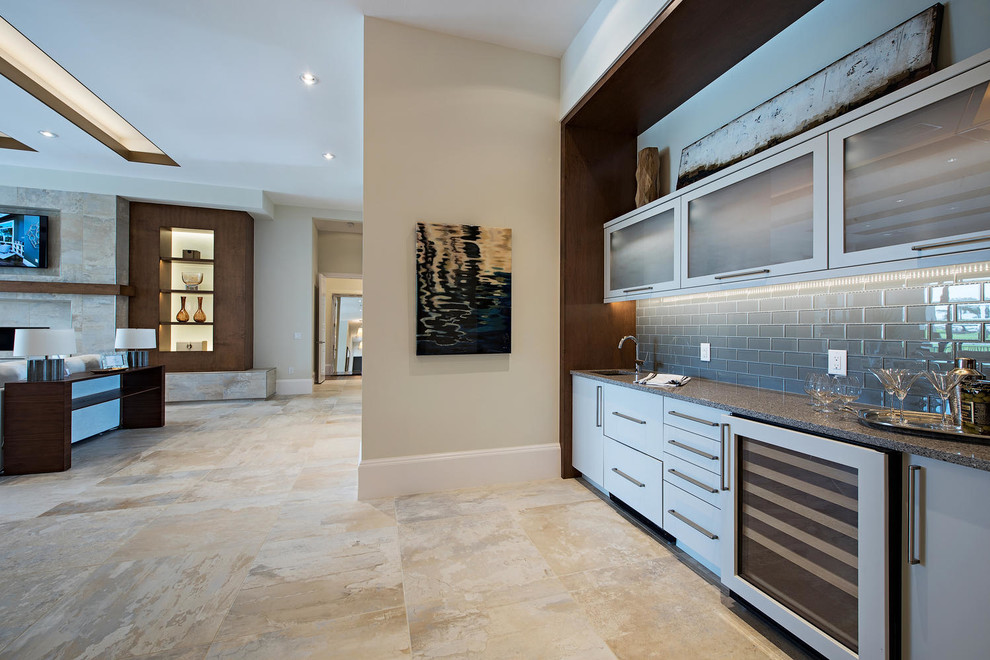 Modern inredning av en mellanstor linjär hemmabar med vask, med en undermonterad diskho, släta luckor, grå skåp, granitbänkskiva, grått stänkskydd, stänkskydd i glaskakel, kalkstensgolv och beiget golv
