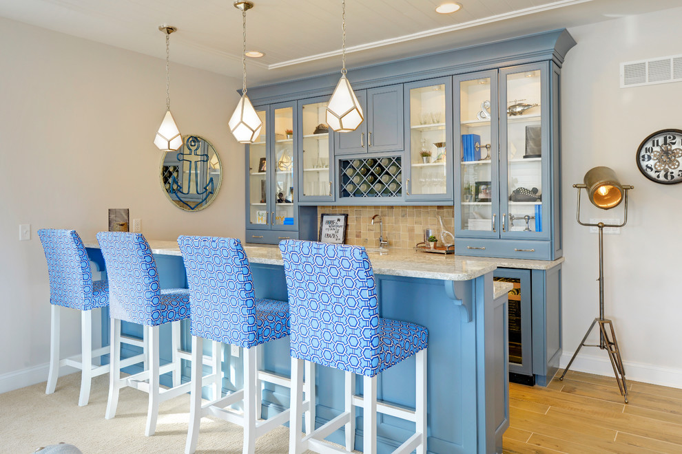 Cette image montre un bar de salon parallèle marin avec des tabourets, un placard à porte vitrée, des portes de placard bleues et une crédence beige.