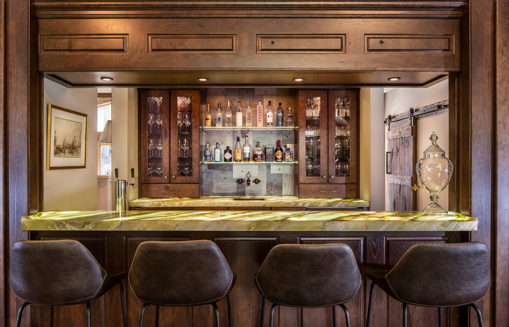 Inspiration for a mid-sized rustic galley brown floor and medium tone wood floor seated home bar remodel in Other with an undermount sink, dark wood cabinets, onyx countertops, gray backsplash, metal backsplash, green countertops and raised-panel cabinets