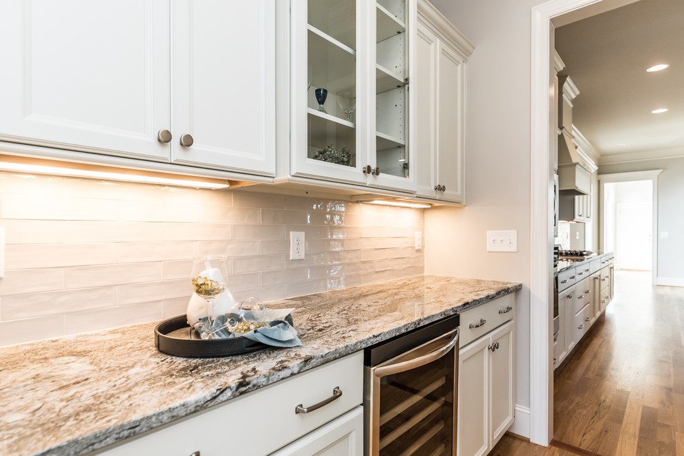 Exempel på en klassisk hemmabar med vask, med släta luckor, vita skåp, granitbänkskiva, vitt stänkskydd, stänkskydd i glaskakel, mellanmörkt trägolv och brunt golv