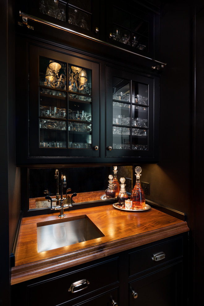 Ispirazione per un angolo bar con lavandino tradizionale di medie dimensioni con lavello sottopiano, ante di vetro, ante nere, top in legno e top marrone