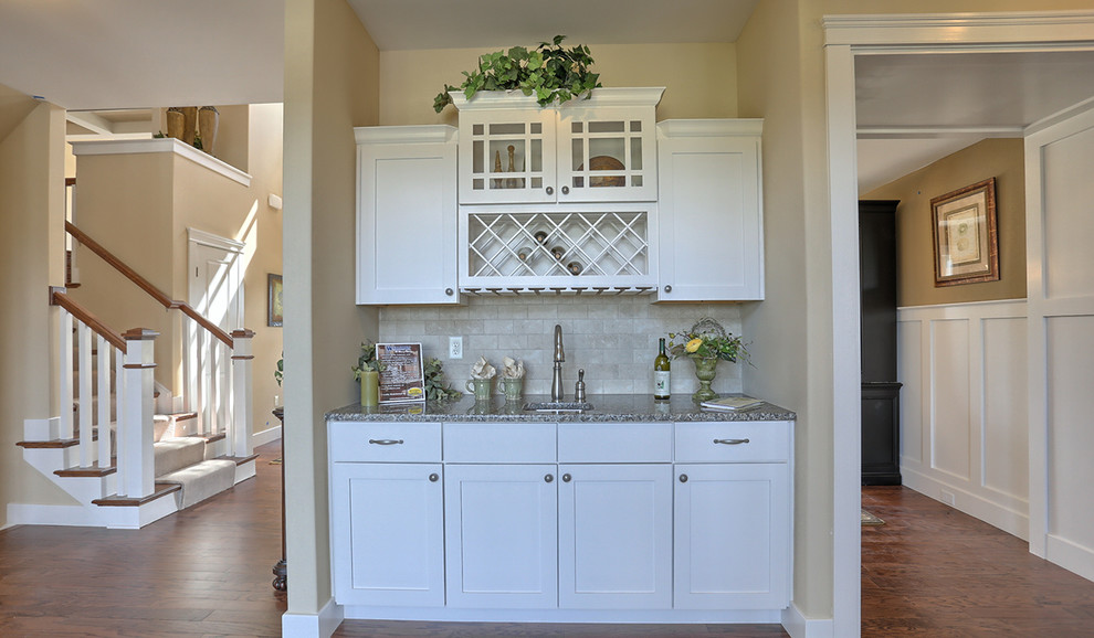 Example of a mid-sized arts and crafts single-wall medium tone wood floor wet bar design in Other with white cabinets, granite countertops, beige backsplash, an undermount sink, shaker cabinets and stone tile backsplash