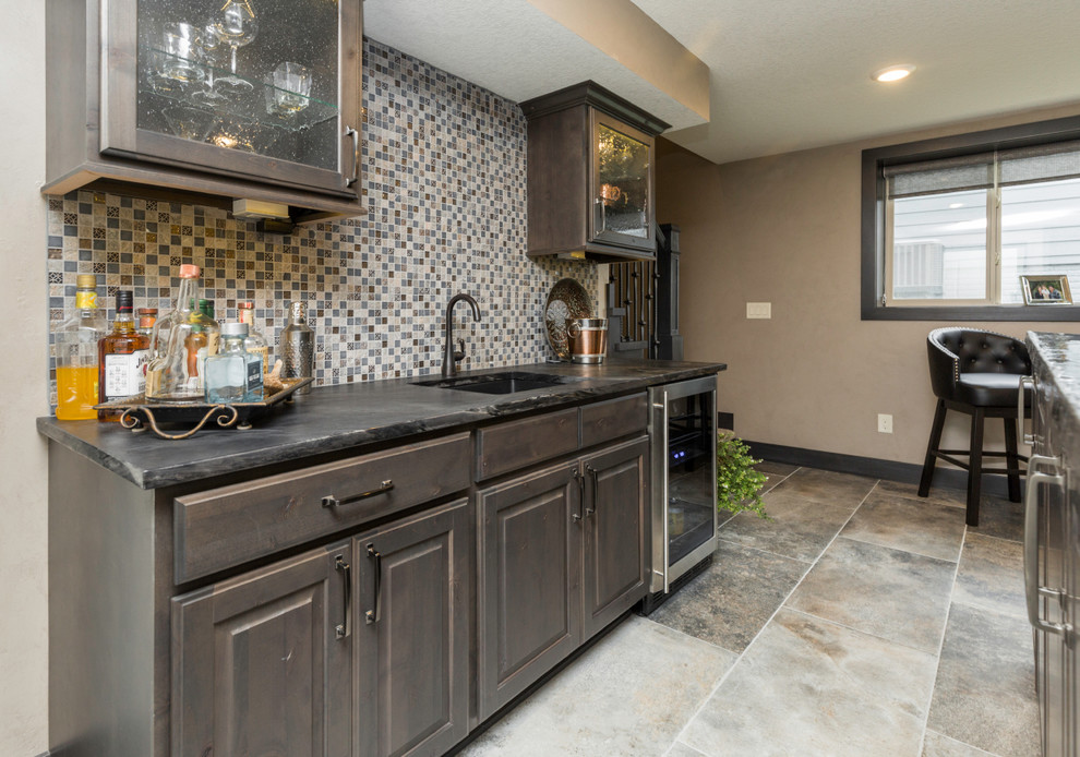 Inspiration for a mid-sized transitional single-wall ceramic tile and gray floor wet bar remodel in Other with glass-front cabinets, dark wood cabinets, granite countertops, gray backsplash, glass tile backsplash and gray countertops