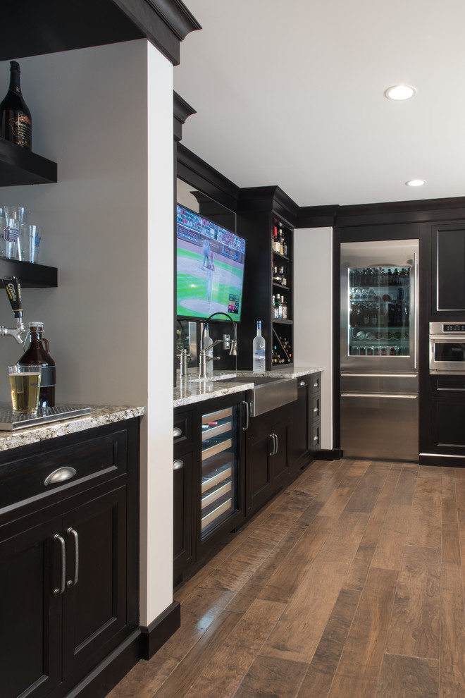 Wet bar - traditional galley brown floor wet bar idea in St Louis with beaded inset cabinets