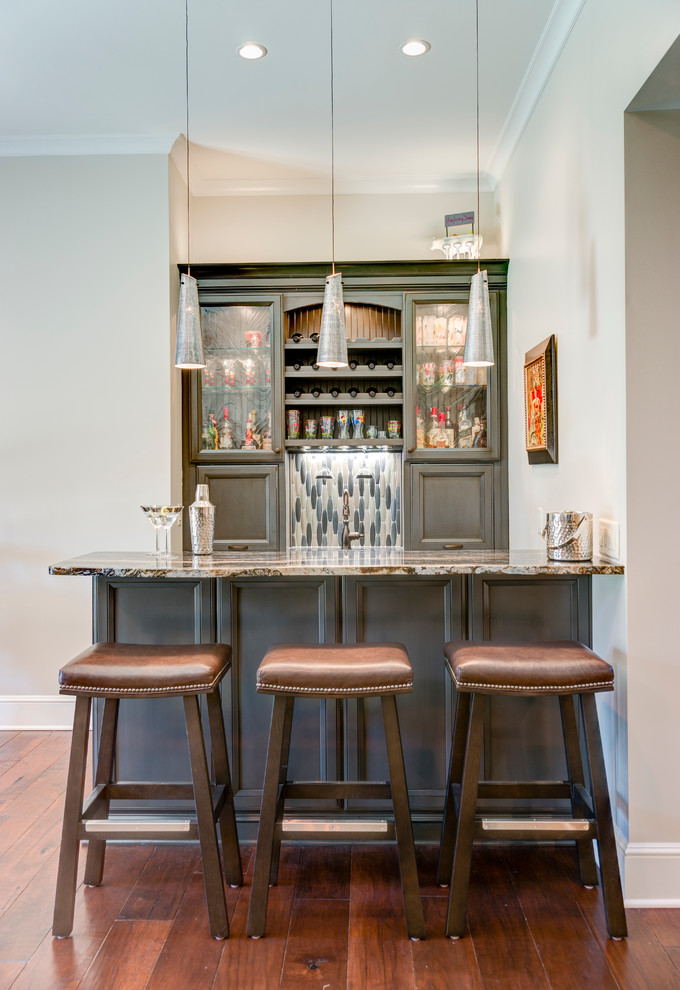 Inspiration for a mid-sized transitional medium tone wood floor seated home bar remodel in Other with an undermount sink, recessed-panel cabinets, gray cabinets, granite countertops, gray backsplash and mosaic tile backsplash