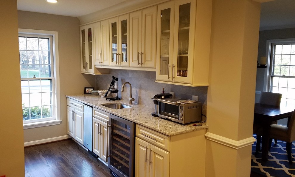 This is an example of a medium sized traditional single-wall wet bar in Baltimore with a submerged sink, raised-panel cabinets, white cabinets, granite worktops, grey splashback, marble splashback, medium hardwood flooring and brown floors.