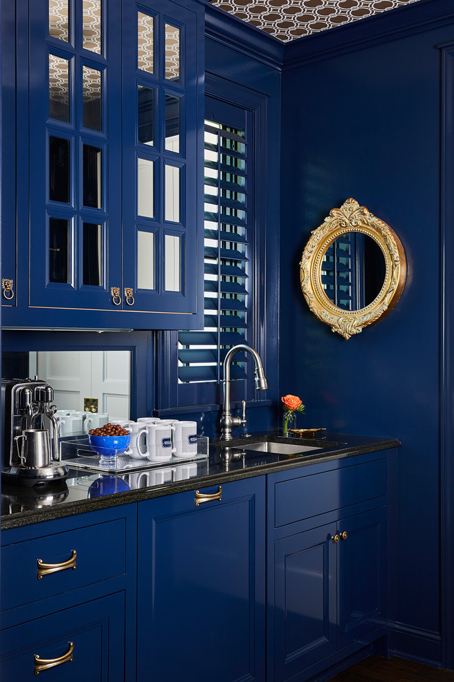 Inredning av en klassisk svarta linjär svart hemmabar med vask, med en undermonterad diskho, luckor med infälld panel, blå skåp och spegel som stänkskydd