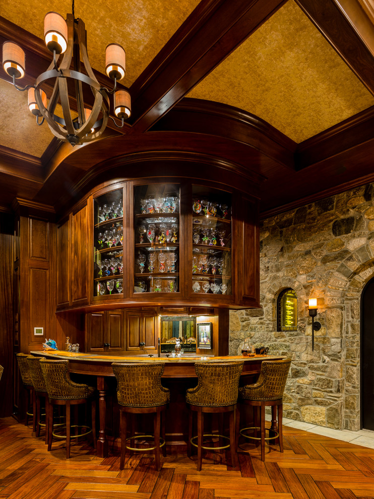 Immagine di un bancone bar mediterraneo con ante in legno bruno, paraspruzzi a specchio, pavimento marrone, top in onice, ante con bugna sagomata e parquet scuro
