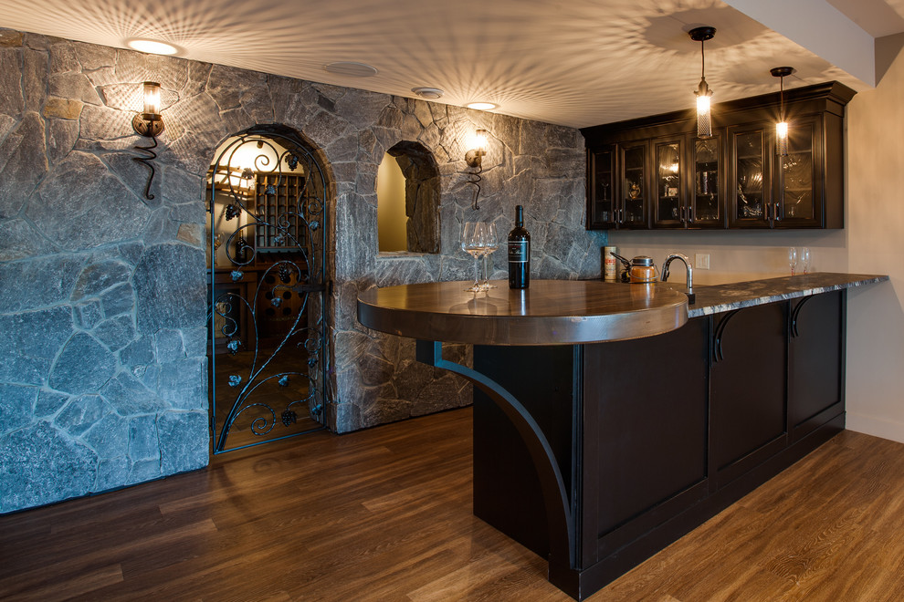 Photo of a mediterranean l-shaped home bar in Vancouver with glass-front cabinets, medium hardwood flooring and brown cabinets.